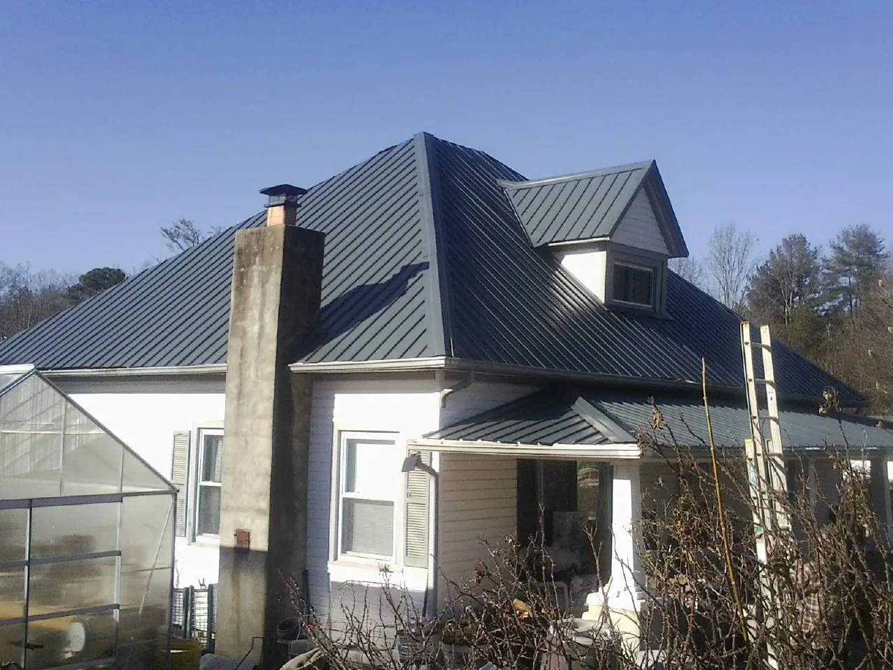 Dark blue standing seam metal roof on a white farmhouse with dormer — Slate & Tile Roof Repair by Roofing Brothers in Barco