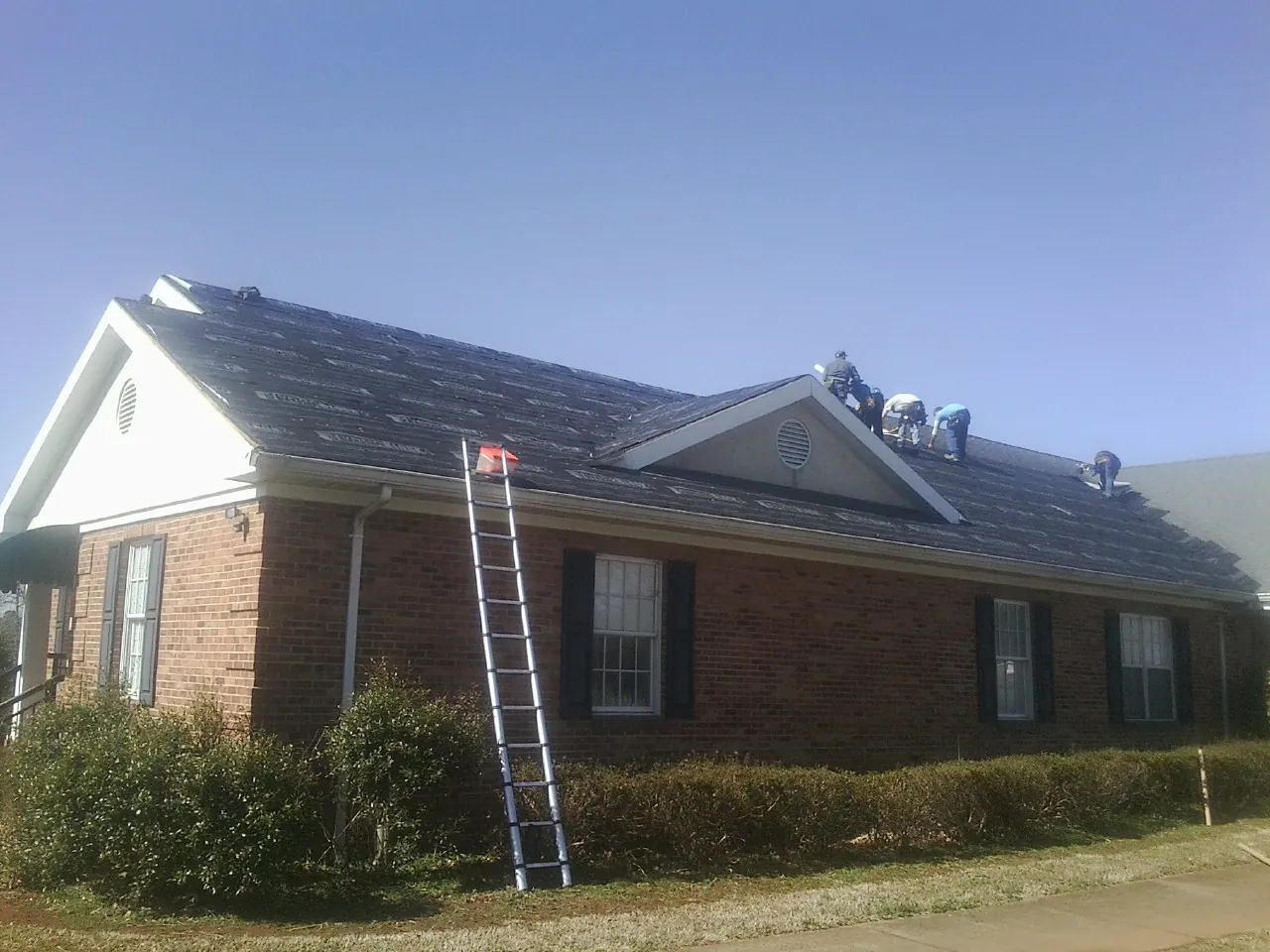 Crew tearing shingles off a brick ranch roof with a ladder set — Emergency Roof Repair work by our crew in Barco