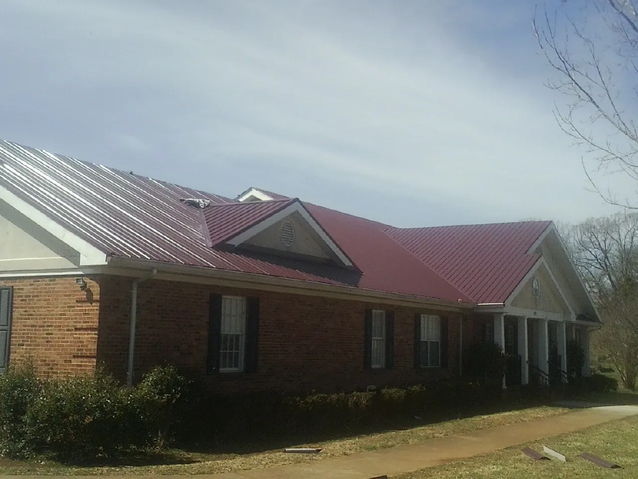 Red metal roof with gabled entries on a long brick building, from a Hail Damage Roof Repair job in Barco