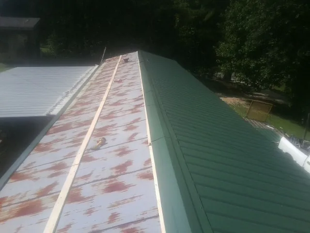 Old rusted panels beside newly installed green metal roofing — Wind Damage Roof Repair by Roofing Brothers in Barco