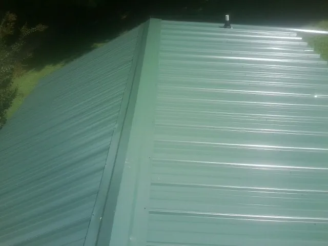 New green metal panels meeting at the ridge of a roof — Flat Roof Repair work by our crew in Barco