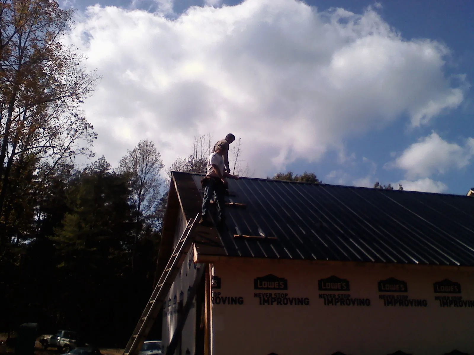 Roofer fastening dark metal panels high against a cloudy sky, from a Roof Inspection job in Barco