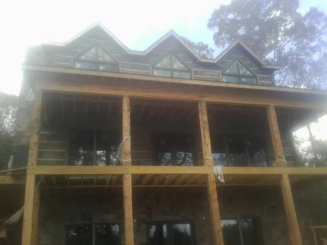 Dormers and porch framing on a large log home under construction — Roof Coating work by our crew in Barco