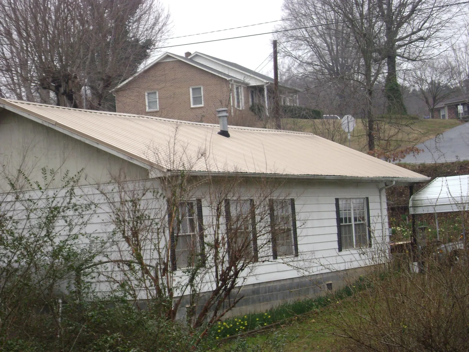 Tan metal roof on a white sided house set into a hillside — Commercial Roofing by Roofing Brothers in Barco
